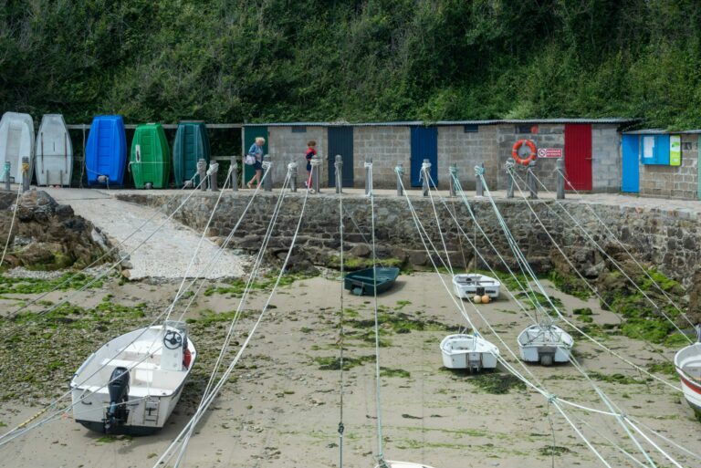 Boats moored at low tide in a Normandy harbor with colorful huts.